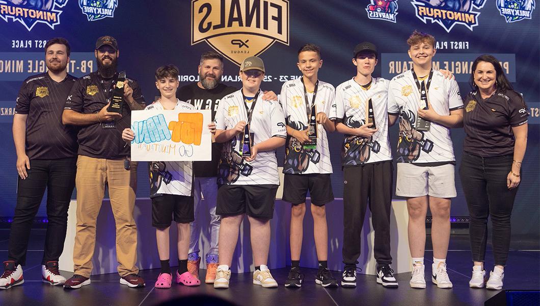 A group of players 和 coaches in esports jerseys on stage, 一名球员举着一个牌子，上面写着“给汉克”.”